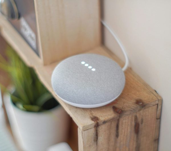 A Google Home Mini smart speaker on a wooden shelf, blending technology with home decor.