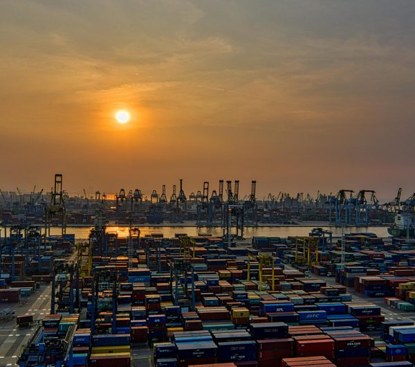 Sunset over a bustling seaport filled with stacked shipping containers and cranes.